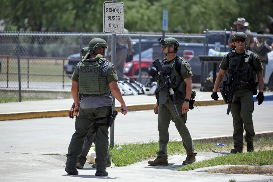 Police in heavy gear stand outside a chainlink fence near a sign that reads: School buses only