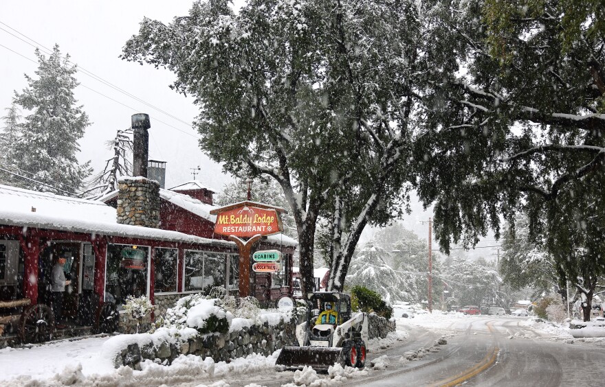 A vehicle clears snow in front of a restaurant as snow falls in the San Gabriel Mountains in San Bernardino County near Los Angeles County, on Feb. 24, 2023 in Mount Baldy, California.