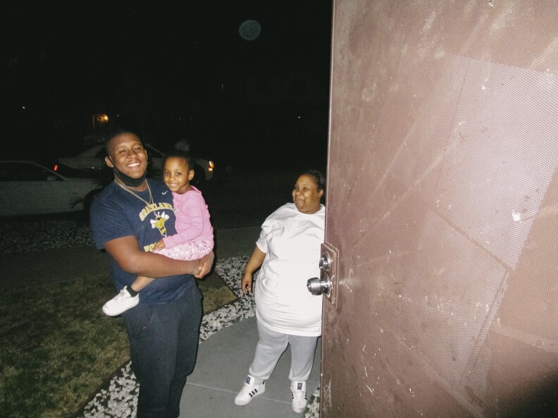 In this image, a man holds a child with a woman standing behind him.