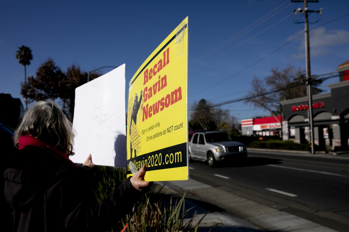 A person holds a bright yellow sign that says in red: Recall Gavin Newsom.