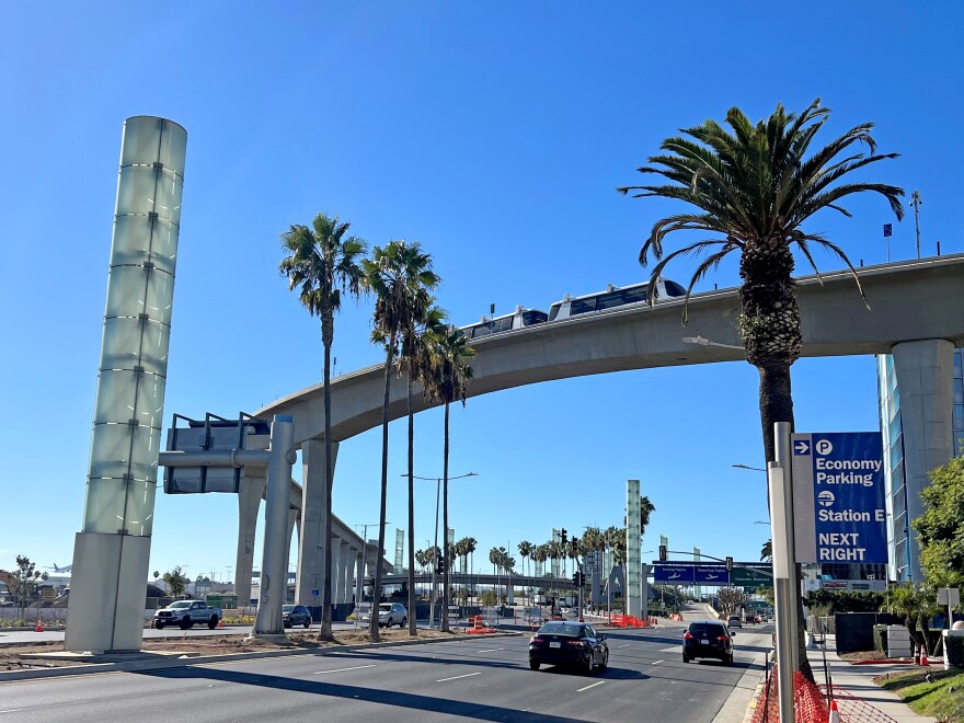 A large concrete bridge spans a wide street on a clear, sunny day, with palm trees rising in the median and on the sidewalk.