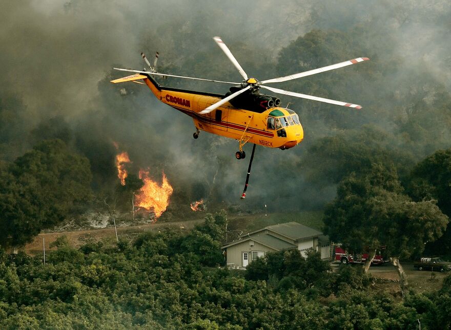 Firefighting helicopters try to save a house from the Thomas wildfire in Carpinteria, California on December 10, 2017.
The Thomas fire is only 15 percent contained, now threatening the city of Santa Barbara and the nearby coastal town of Carpinteria, making it one of the worst wildfires in California history.
 / AFP PHOTO / MARK RALSTON        (Photo credit should read MARK RALSTON/AFP/Getty Images)