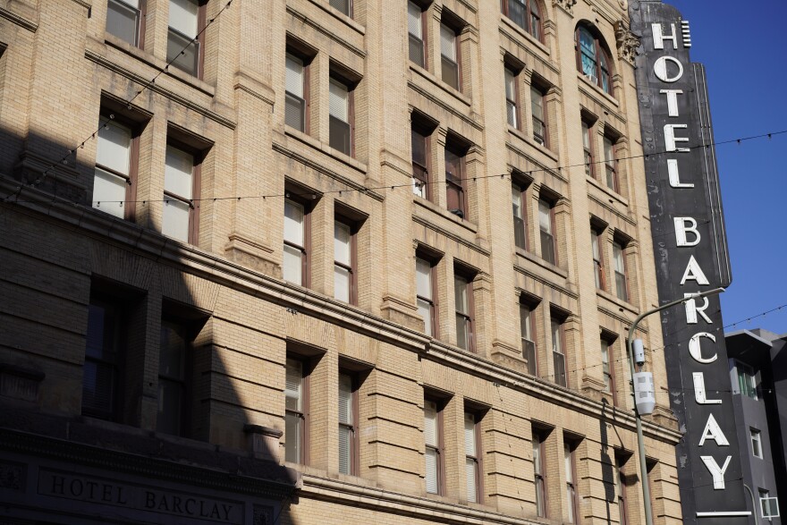 A shadow begins to cover the outer wall of the Barclay Hotel. A large vertical sign on the corner of the building says "Hotel Barclay" in an Art Deco font.