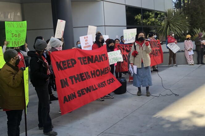 Tenants and organizers from Hillside Villa -- a Chinatown low-income housing complex -- stage a protest outside Los Angeles Housing Department on March 7, 2023 against general manager Ann Sewill. Two protesters in the center hold a red banner that says "KEEP TENANTS IN THEIR HOMES. ANN SEWILL MUST GO!" A young Asian woman speaks into a microphone on their right. Other protesters holding posters surround them.