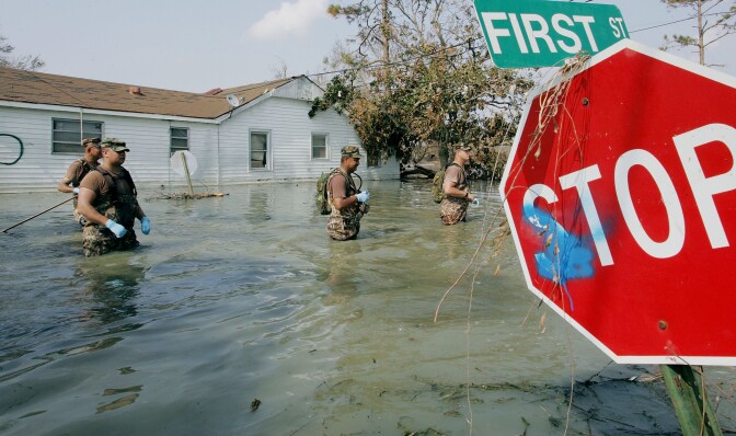 Men in uniform stand in waist deep water.