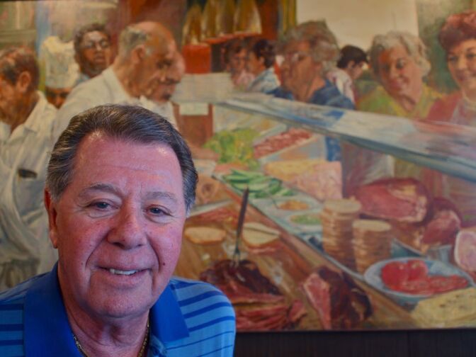 Norm Langer in front of the Marinus Welman's painting of Langer's Deli. Norm's father appears in the far left and Norm himself makes an appearance toward the top right.