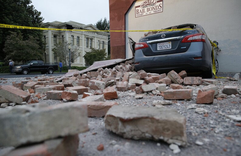 Bricks and fallen rubble cover a car with the old courthouse in the background following an earthquake Sunday, Aug. 24, 2014, in Napa, Calif. A large earthquake rolled through California's northern Bay Area early Sunday, damaging some buildings, igniting fires, knocking out power to tens of thousands and sending residents running out of their homes in the darkness.