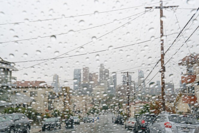 View of the downtown Los Angeles skyline from behind a rain-soaked car windshield.