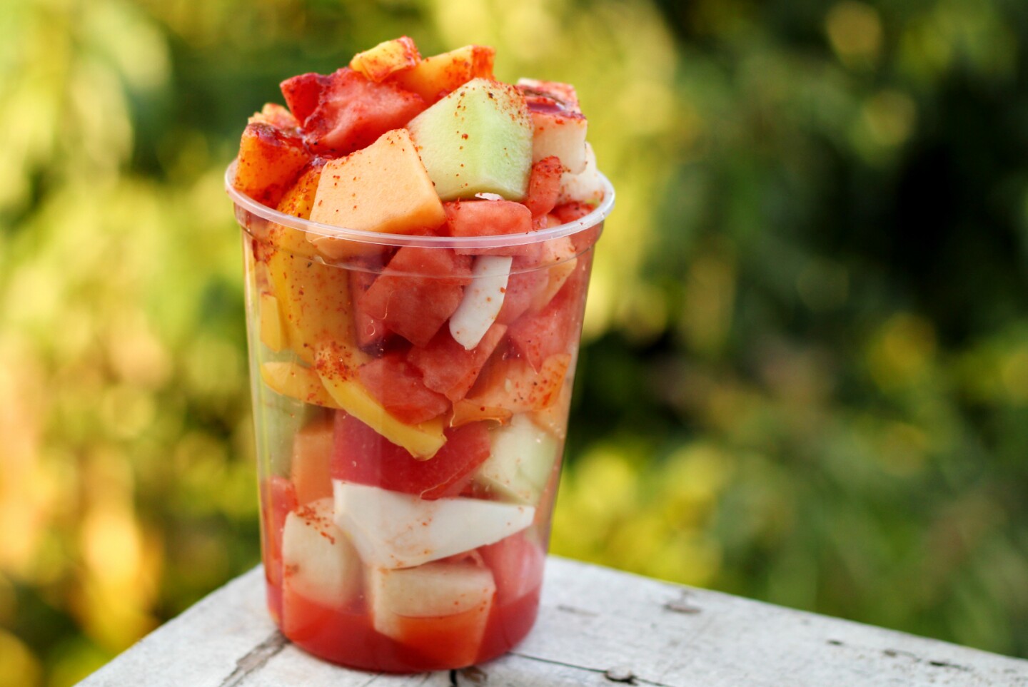 a plastic cup of cut-up watermelon, honeydew, cantaloupe, coconut and mango sprinkled with a red spice.