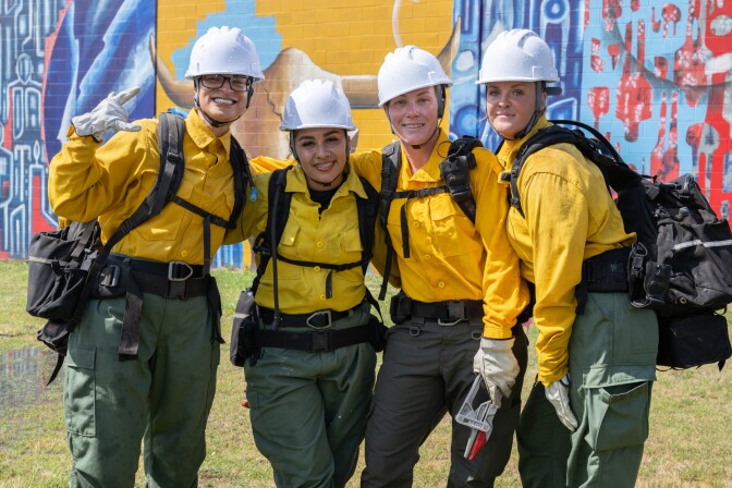 Four women pose wearing firefighting gear.