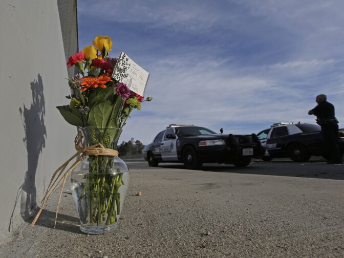 Flowers are left by the side of the road as a San Bernardino police officer blocks the road leading to the site of yesterday's mass shooting on Thursday, Dec. 3, 2015 in San Bernardino, Calif.  A heavily armed man and woman dressed for battle opened fire on a holiday banquet for his co-workers Wednesday, killing multiple people and seriously wounding others in a precision assault, authorities said. Hours later, they died in a shootout with police. (AP Photo/Chris Carlson)