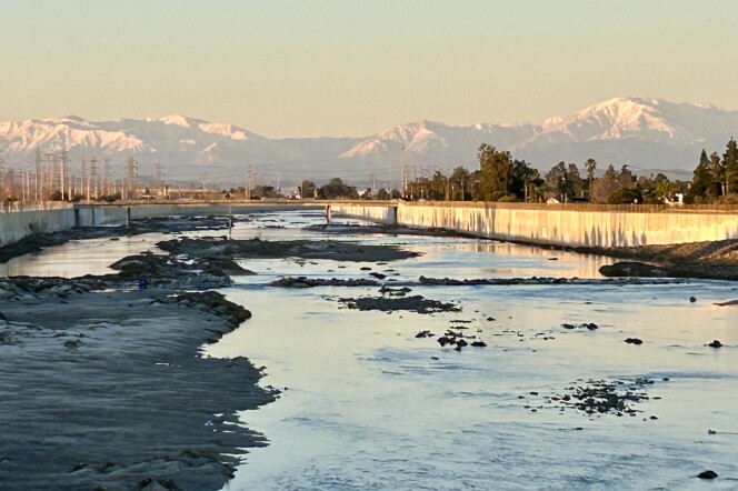 Snow capped mountains are in the distance as the golden hour sun reflects on a river with concrete embankments.