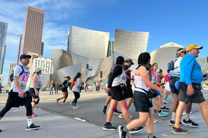 Runners and walkers running past a silver building in odd shape