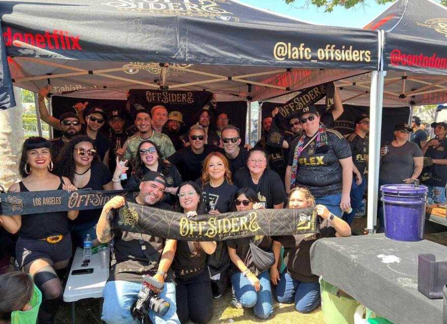 A group of men and women dressed in mostly black a gathered and holding a banner that says "Los Angeles Offsiders"
