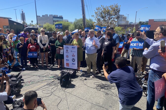 A crowd of people surrounds Los Angeles Mayor Karen Bass, who stands at a podium.