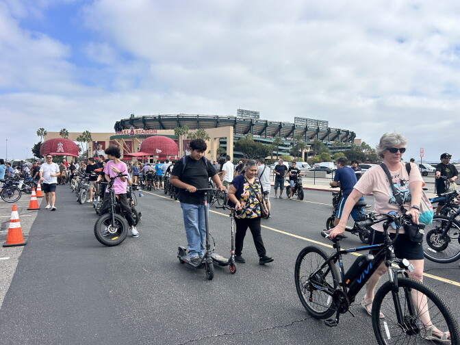 People with bikes and scooters gather in a parking lot outside Angel Stadium in Anaheim.