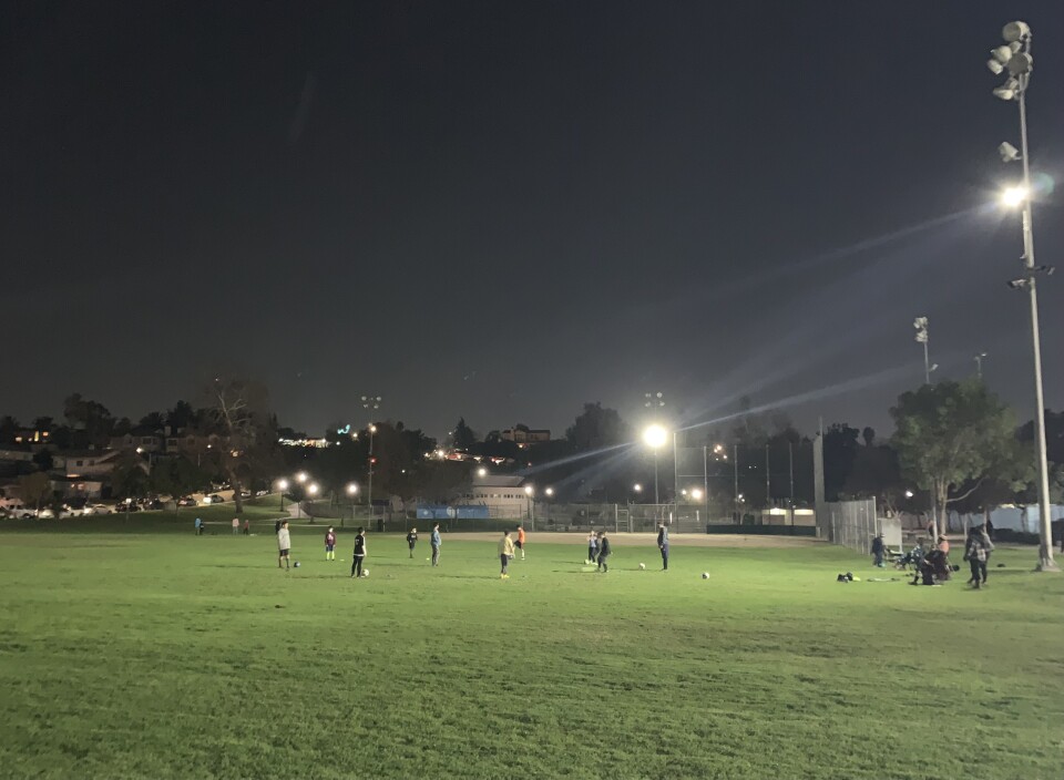 A nighttime scene of about a dozen kids playing soccer at a park.