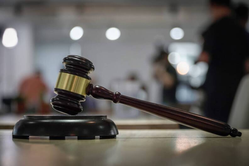 A close-up of a judge’s gavel resting on its block in a courtroom.