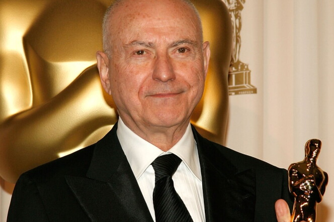 A man with light-tone skin holds an Oscar statuette. His head is bald on top.