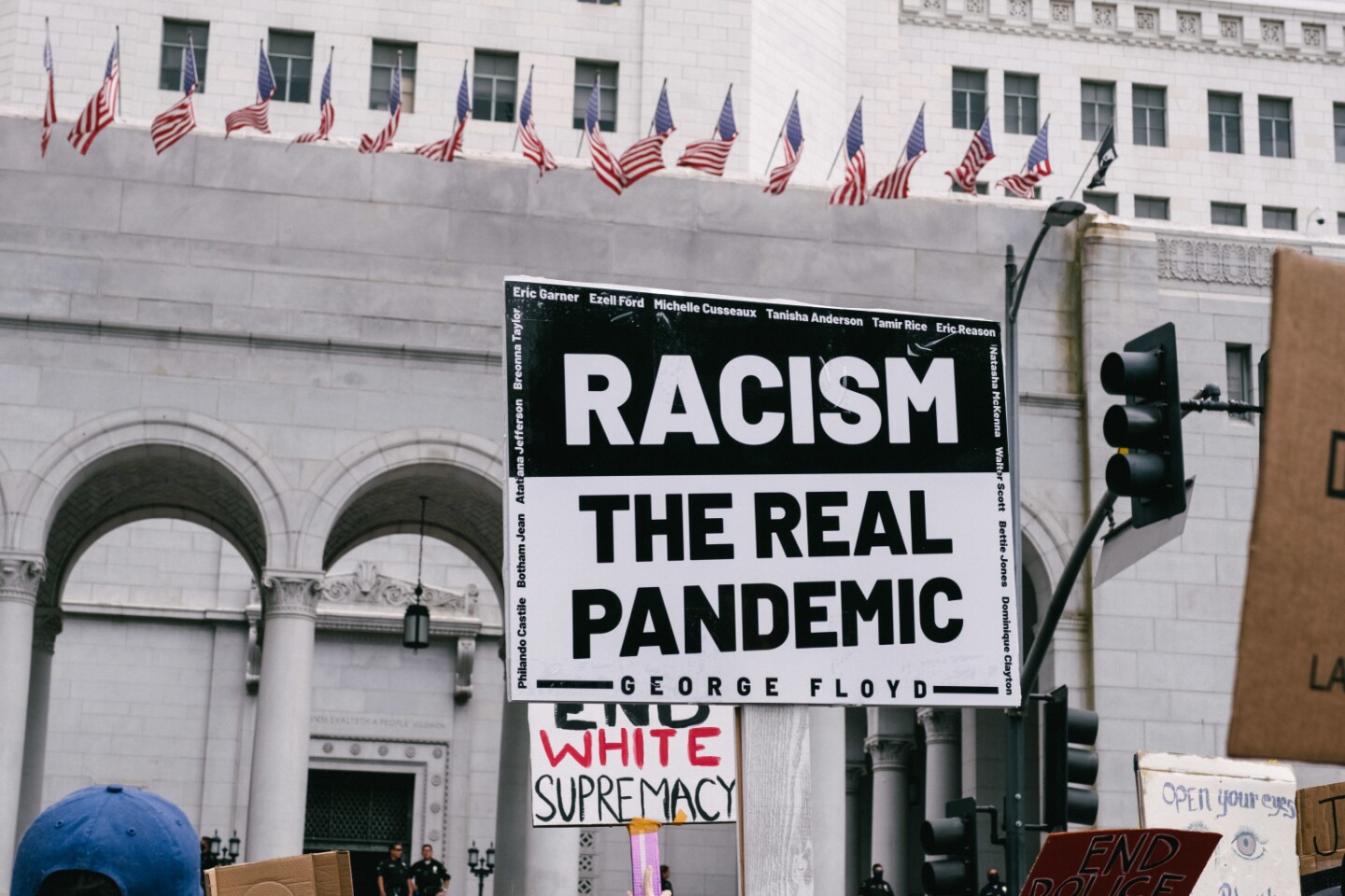 A sign at a protest in front of City Hall reads "Racism- The Real Pandemic."