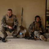Two men sit side by side in army gear. 