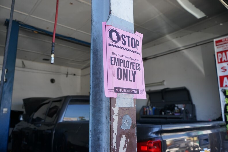 A pink paper sign is duct-taped to a metal pole. It reads: "STOP - This is a Private Space for EMPLOYEES ONLY - NO PUBLIC ENTRY." Behind the pole, there's a truck with it's hood open.