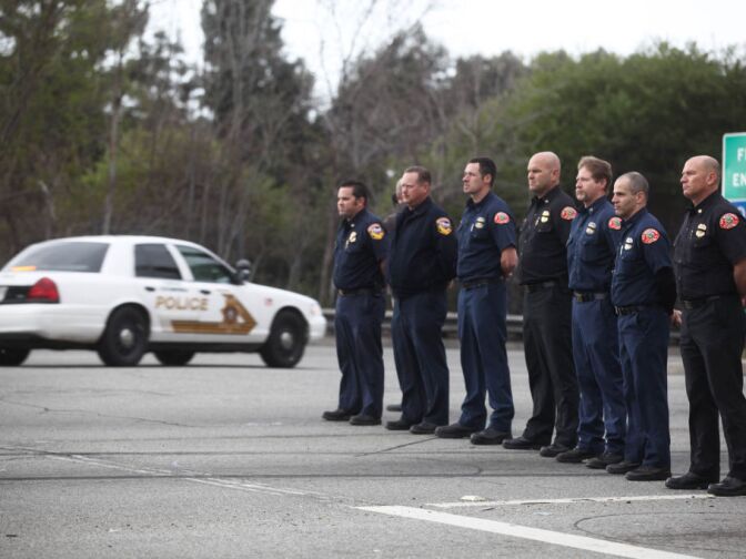 A fire truck crew stands at attention near the I-210 on ramp as the funeral procession for Det. Jeremiah MacKay passes by.