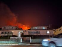 A night sky is deep red with flames and smoke behind an apartment building.