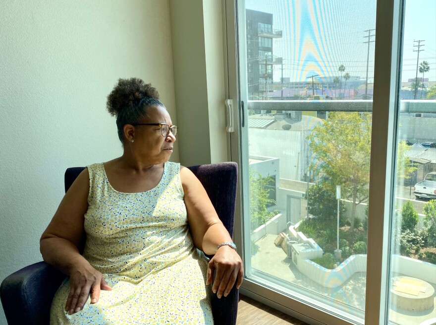 Lisa Chilton wears a flower-print sun dress as she sits in a chair in her living and looks out the window.