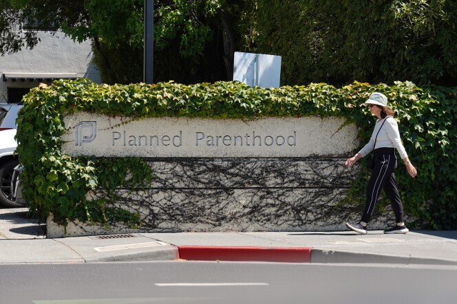  A woman wearing a hat walks past a Planned Parenthood sign on a sidewalk.