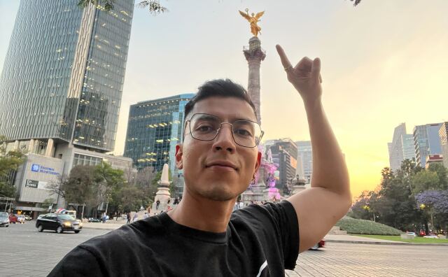 A young Latino man with glasses in Mexico City in front of the Angel de Independencia