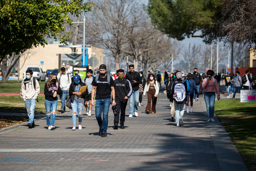 Students wearing masks walk on a path under trees.