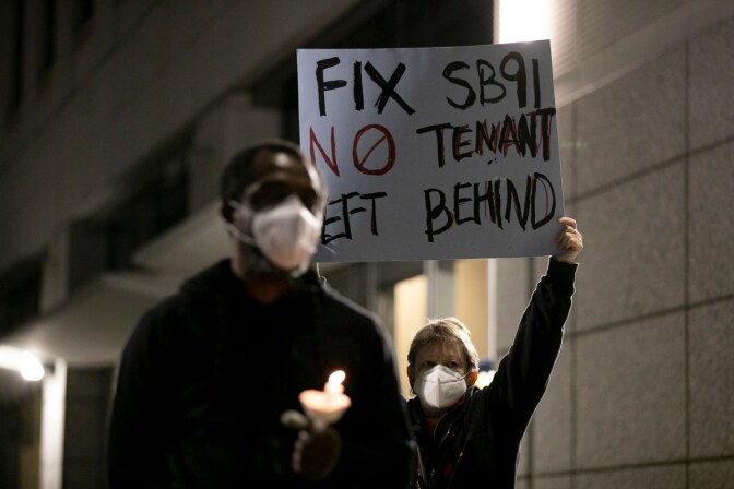 A masked protester holds up a sign reading Fix SB91 No Tenant Left Behind