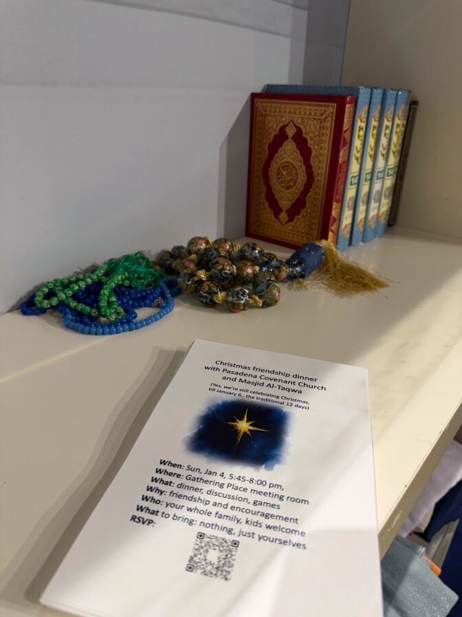 Qur'ans in jewel tones with gold embossed detailing on the cover alongside different colored prayer beads and a flyer for an interfaith lunch. 