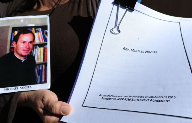 Esther Miller holds a picture and the released documents on Reverand Michael Nocita as victims and their supporters hold quilts bearing portraits of abused children while gathered outside the Cathedral of Our Lady of the Angels in Los Angeles, California, on February 1, 2013, one day after the release of personnel files of priests accused of sexual misconduct. The archbishop of Los Angeles Jose Gomez stripped his predecessor, retired Cardinal Roger Mahony, of all church duties on January 31. In all, 124 files were released on the Los Angeles archdiocese's website, listed by priests' names, including 82 containing information on allegations of childhood sexual abuse.