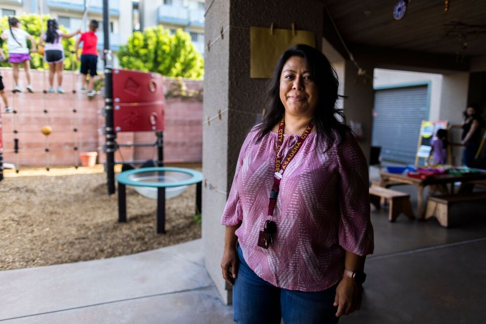 PCC day care director stands in children's play area with little tables and children climbing playground toys.