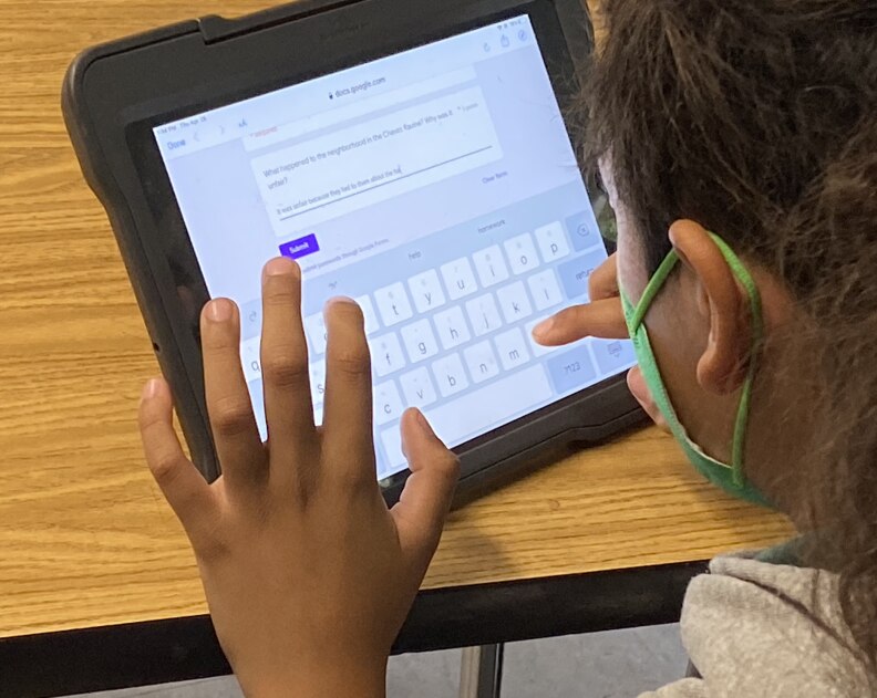 A sixth grader taps the screen of a tablet computer which is currently displaying a keyboard and a Google Form.
