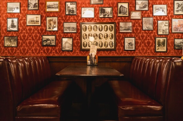 A pair of deep red leather booths sit across from each other in a warmly lit corner of Cole’s, flanked by a wall of vintage black-and-white photographs and a red damask wallpaper.