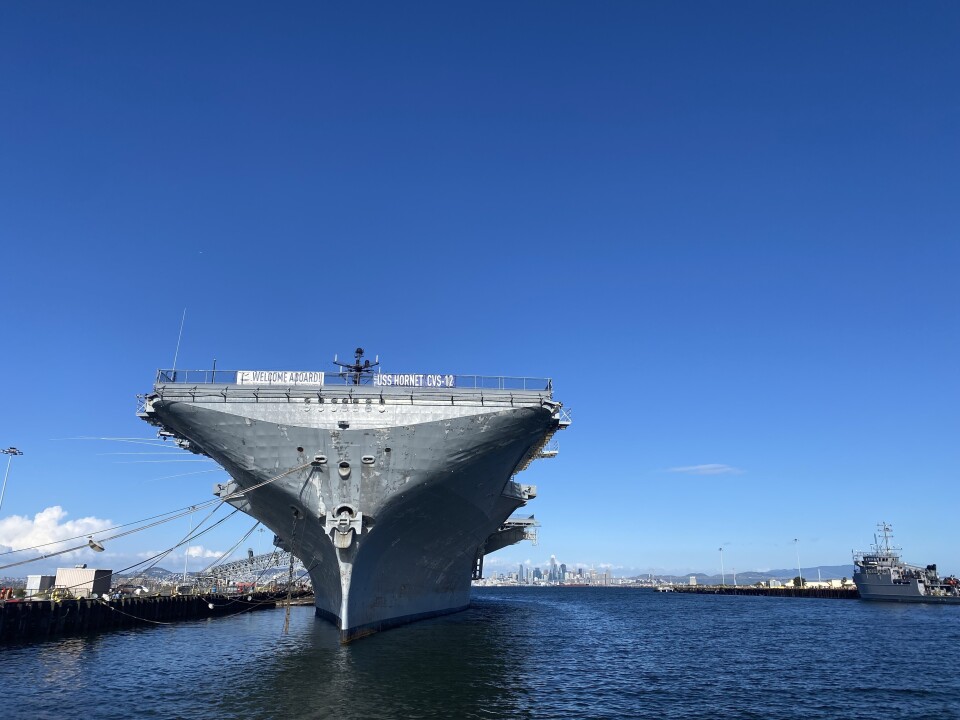An aircraft carrier sits in the water tethered to a dock