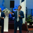 A man with a microphone speaks in a church building to a crowd.