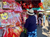 A woman in a hat, her back to the camera, browses Lunar New Year decorations on a busy street. 
