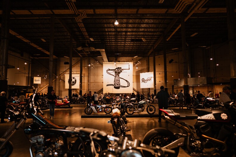 Open room filled with over 20 motorcycles and people walking by