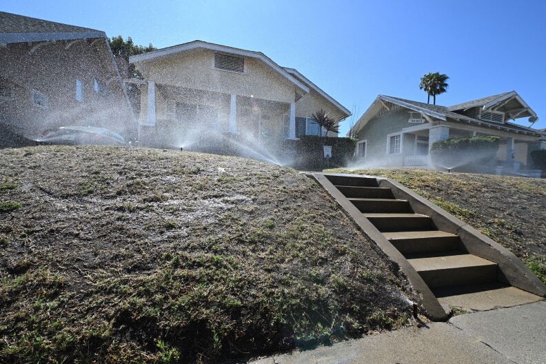 Multiple sprinklers spray a lawn in frony of a bungalow
