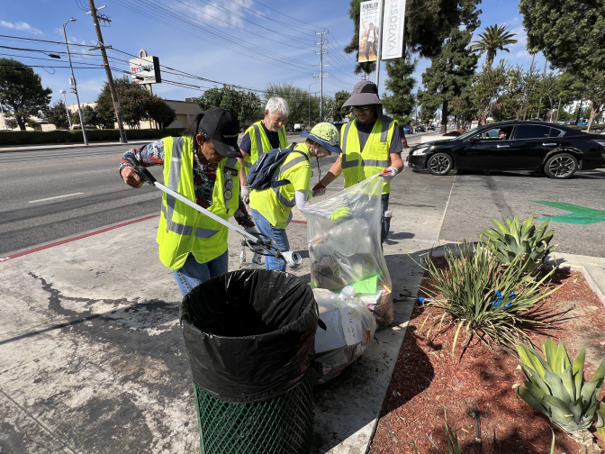 Four members of the Volunteers Cleaning Communities gather around a trash can. Three of them are consolidating trash collections into one bag. One of them is collecting recyclables to take to a local recycling center.