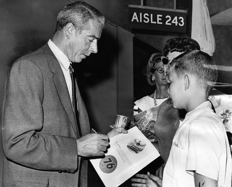 1963: "Dapper Joe DiMaggio signs autograph for young fan on visit last season to Dodger Stadium."