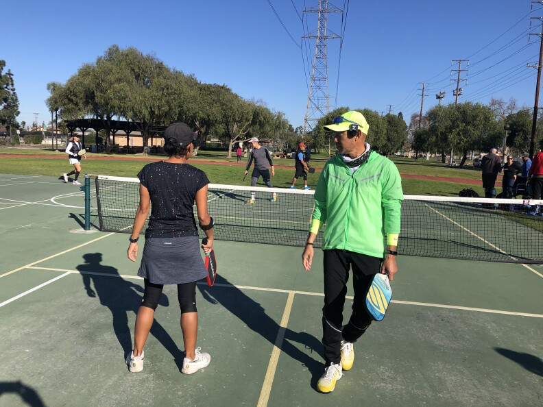 A woman and man holding pickleball paddles on a court