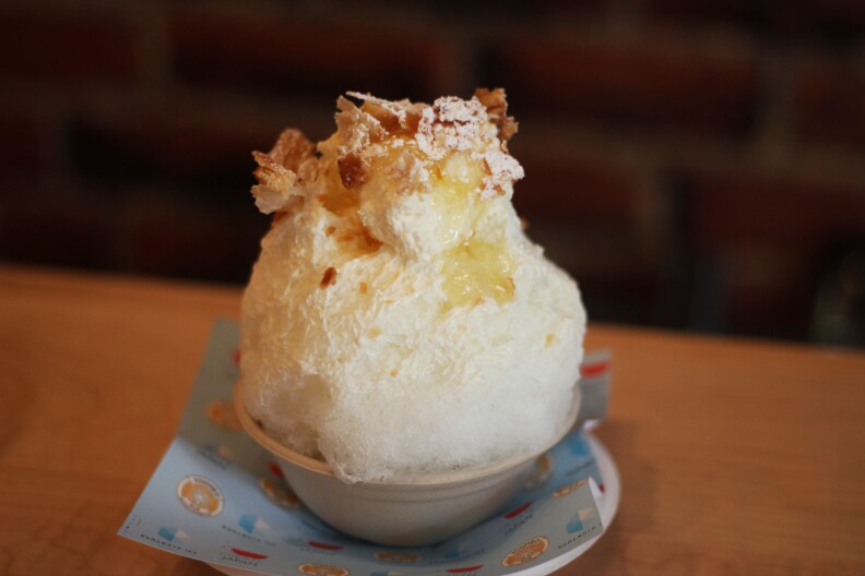 a mound of white shaved ice and cream topped with toast brown flakes
