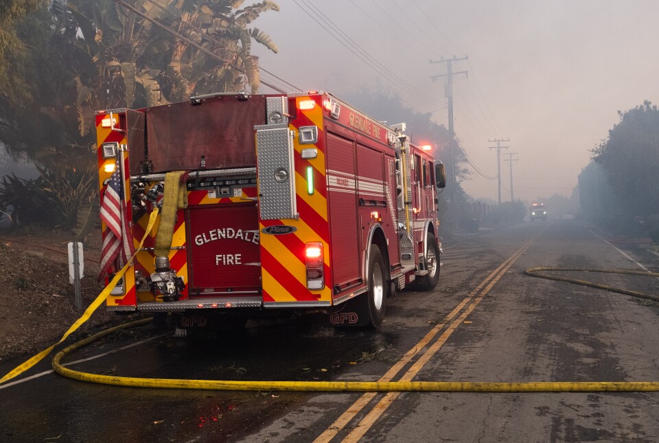 A red fire truck with a yellow hose sneaking across a street. 