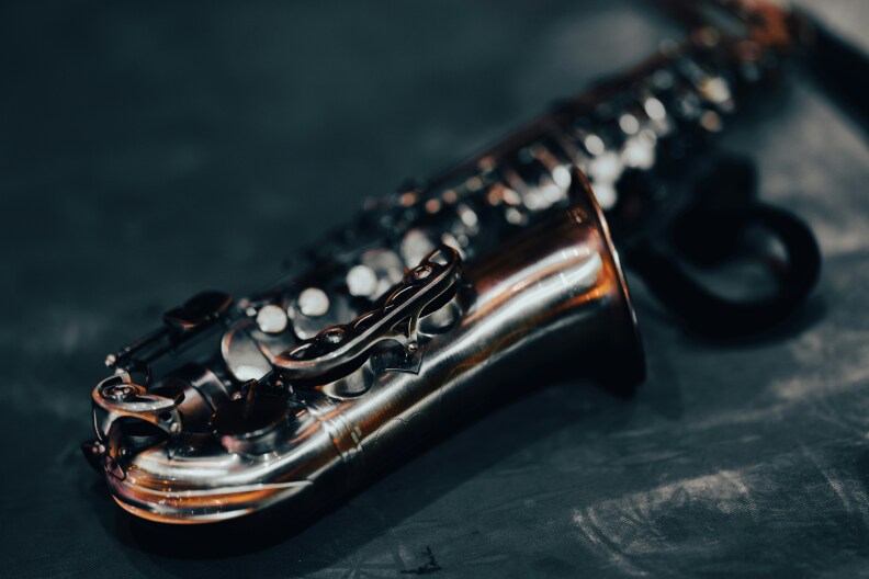 A saxophone lies on a slate gray table in moody lightining.