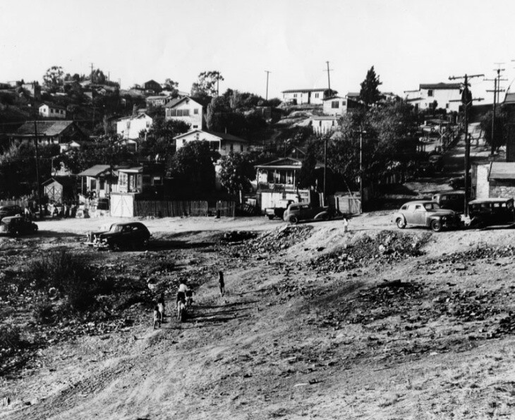 People climb a dirt hill in the foreground toward houses on the hillside